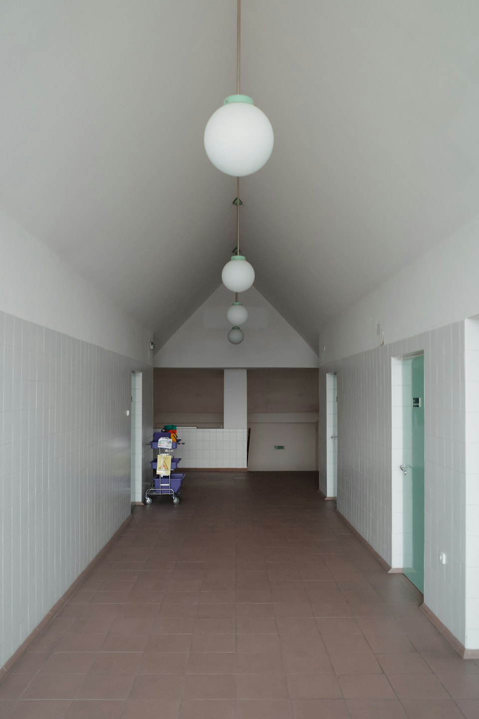 Cleaning cart sitting in a long hallway with pendant lights.