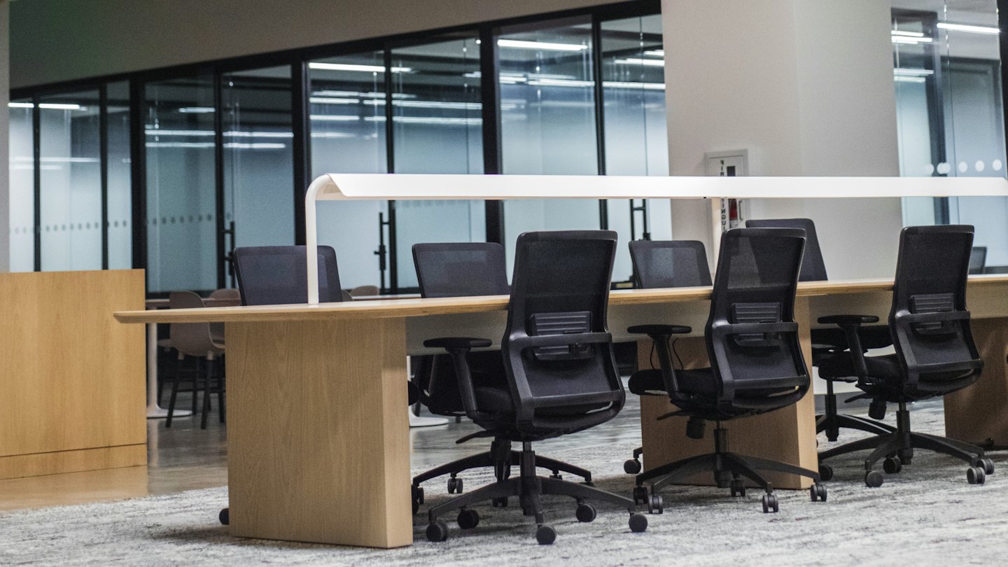 Modern empty office with light wooden desks and black chairs.
